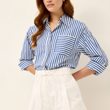 Woman wearing a blue and white striped shirt and white shorts on a beige background