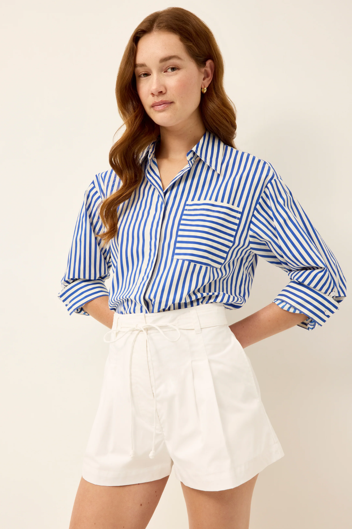 Woman wearing a blue and white striped shirt and white shorts on a beige background