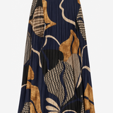 A pleated midi skirt featuring an abstract botanical pattern in navy blue, tan, beige, and black, shown against a plain light gray background.