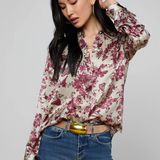 Woman wearing a floral blouse and blue jeans with a gold belt on a gray background