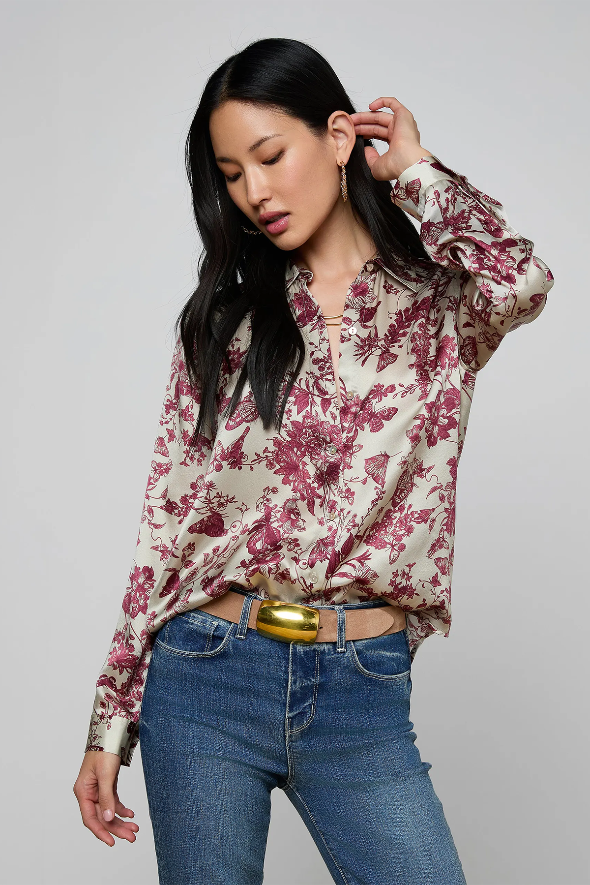 Woman wearing a floral blouse and blue jeans with a gold belt on a gray background