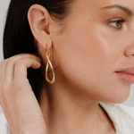 Close-up of a woman wearing a gold earring with a white shirt.