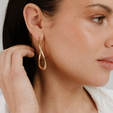 Close-up of a woman wearing a gold earring with a white shirt.