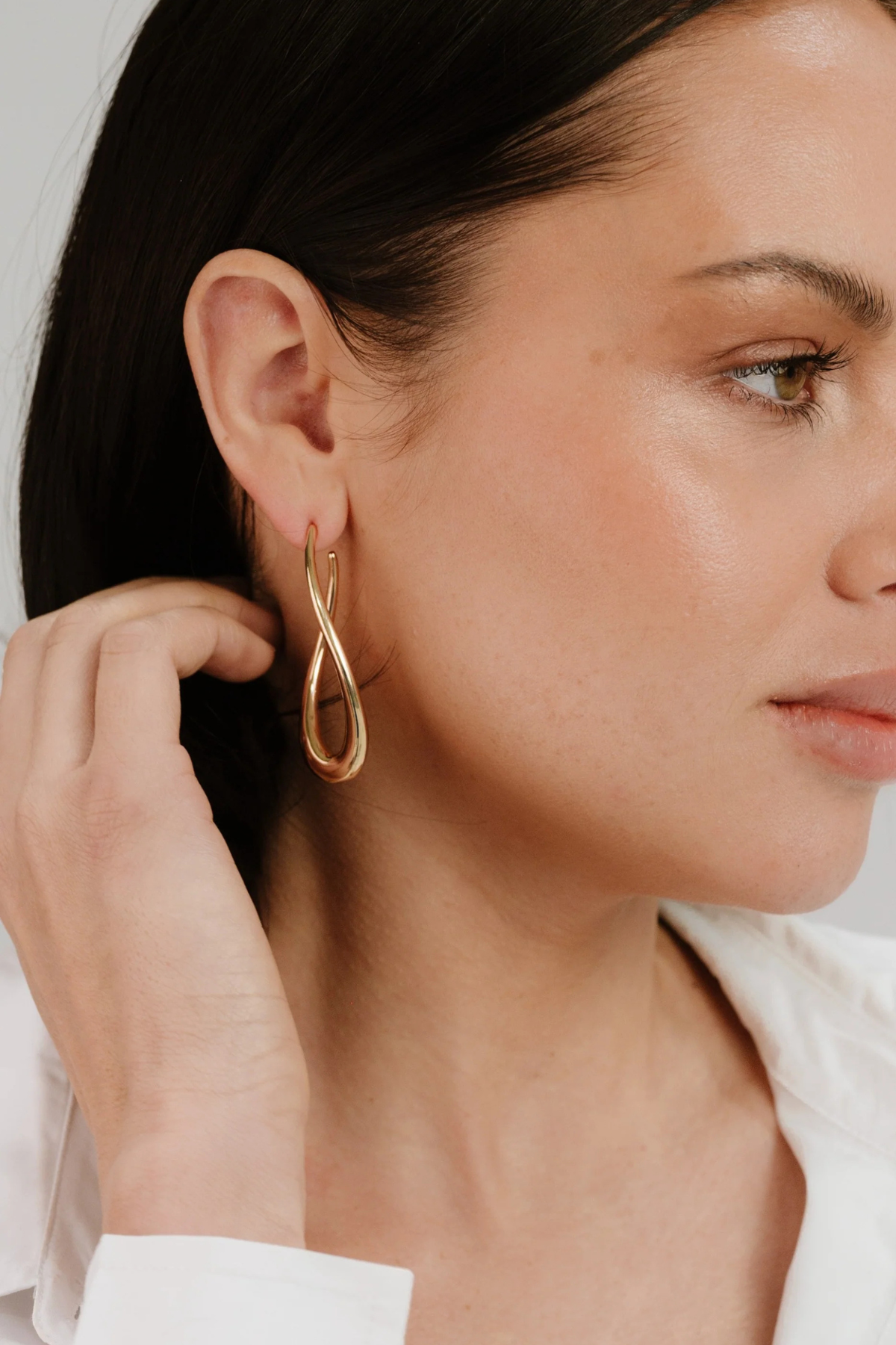 Close-up of a woman wearing a gold earring with a white shirt.