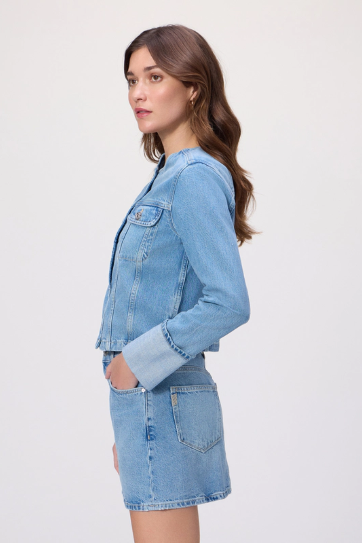 Woman wearing a light blue denim jacket and skirt on a white background