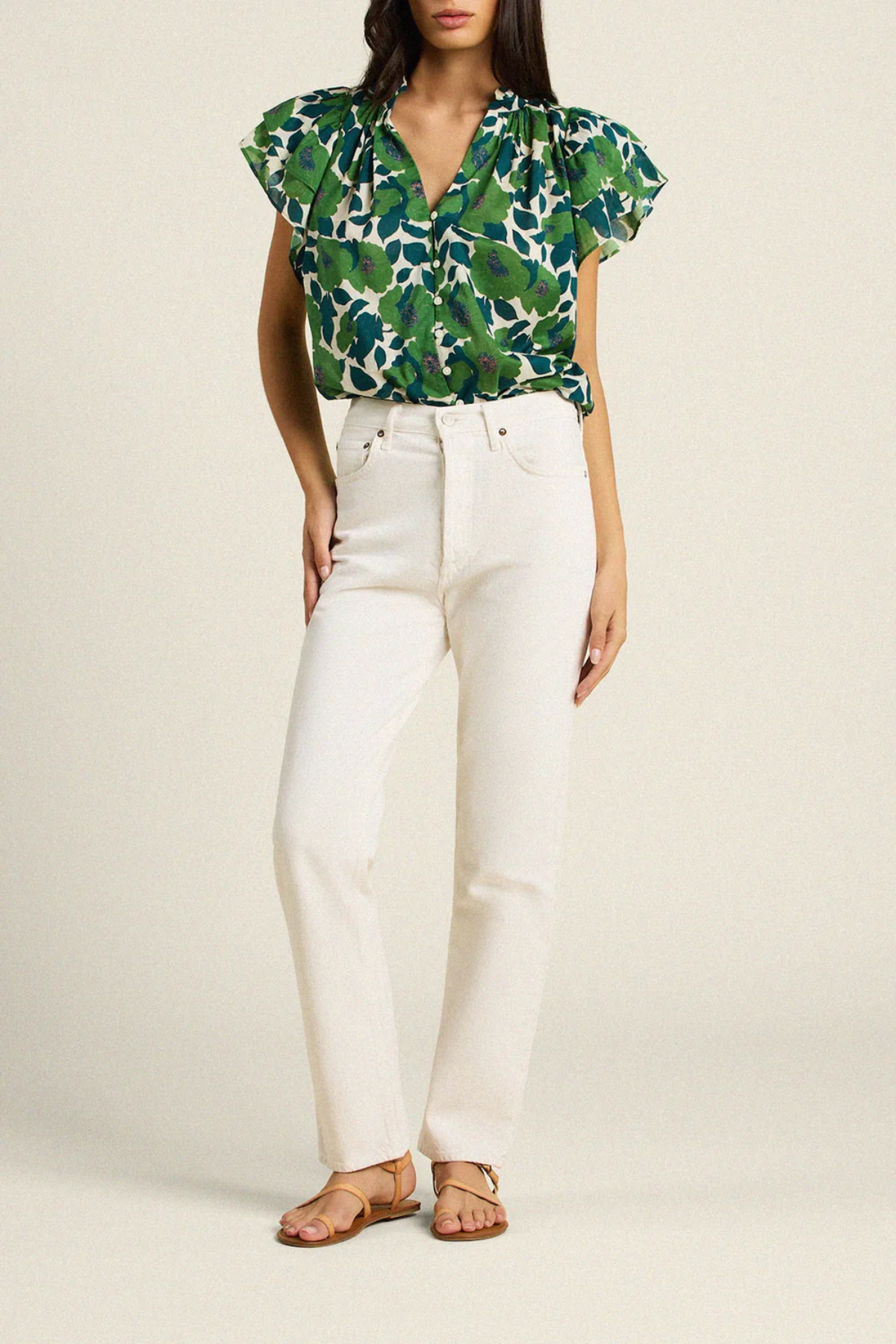 woman in green floral blouse and white denim on tan background 