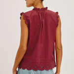Woman wearing a burgundy sleeveless top with ruffle details and light blue jeans on a plain background