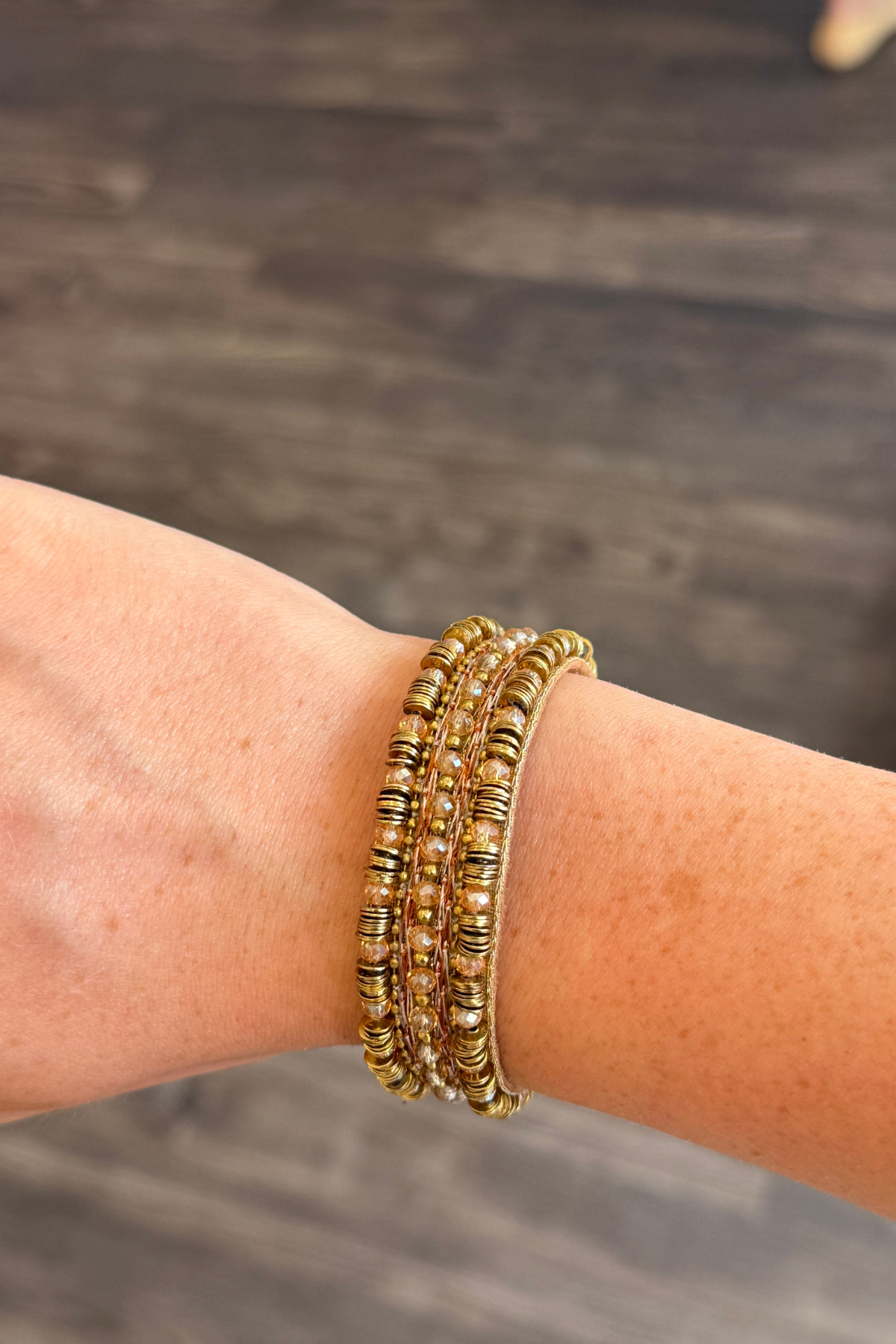 Beaded bracelet shown on someone's wrist featured on a blurred dark background.