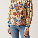 A woman wearing a long-sleeve high-neck blouse with a colorful abstract floral pattern in beige, blue, brown, and orange, paired with light-wash blue jeans against a plain light background.