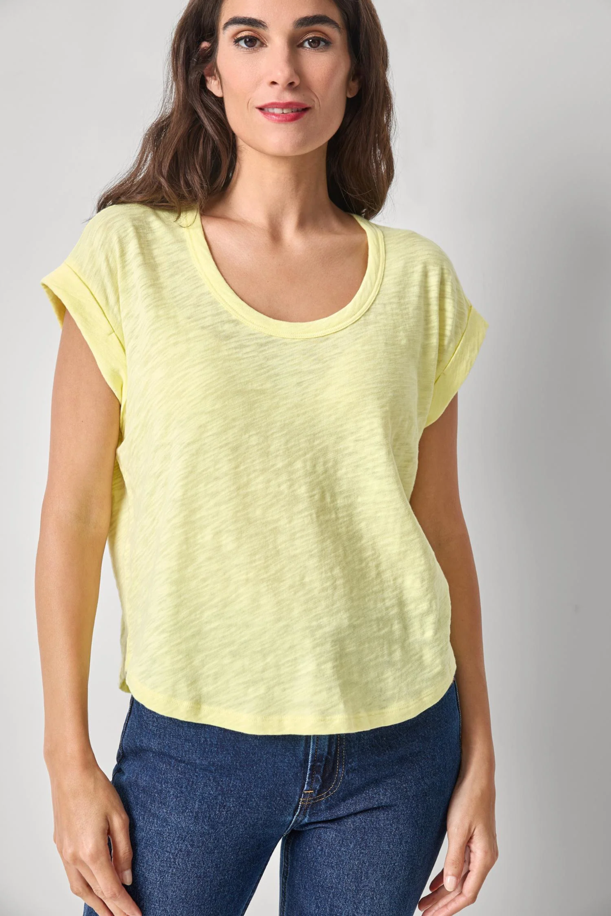 Woman wearing a yellow top and blue jeans against a plain background