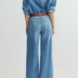 Person wearing a denim outfit with wide-leg jeans and a belt on a light gray background