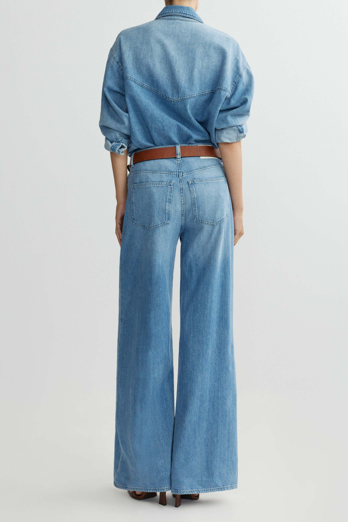 Person wearing a denim outfit with wide-leg jeans and a belt on a light gray background