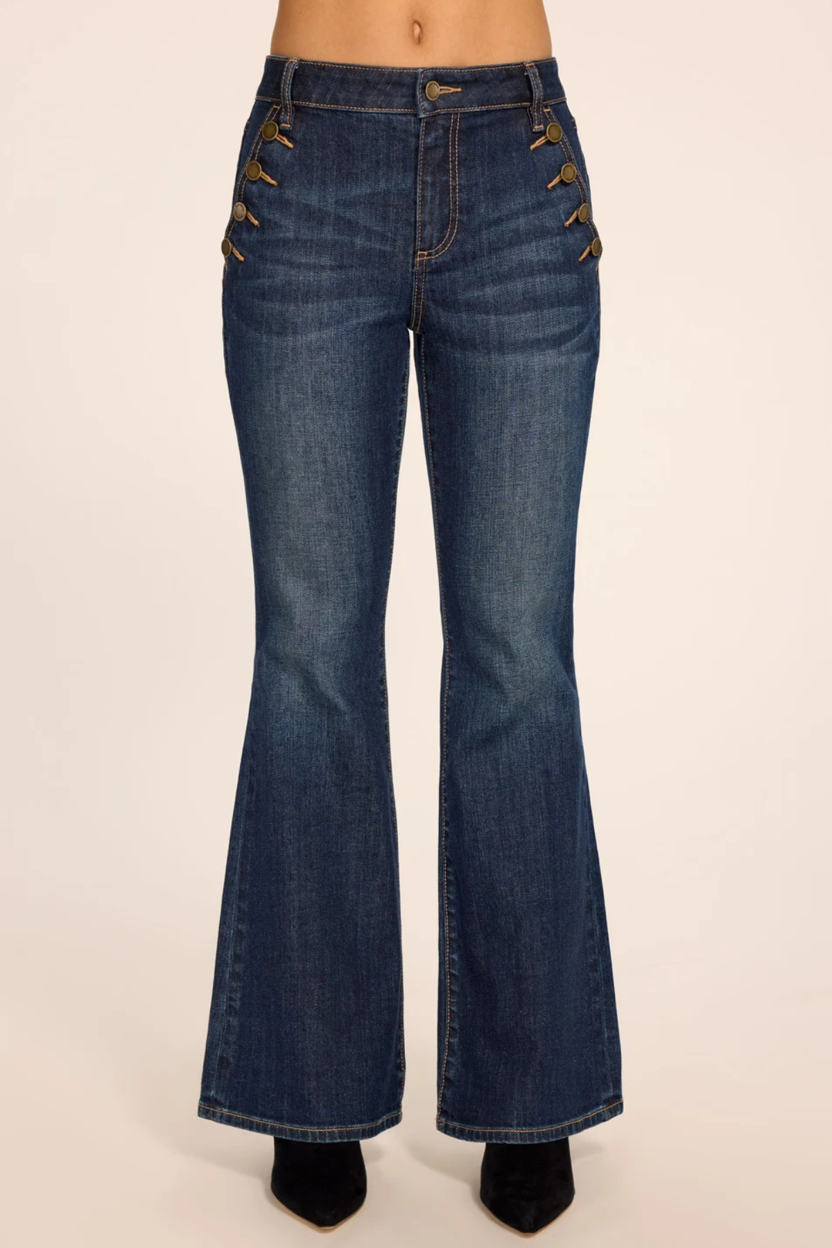 Medium wash blue denim flare jeans with decorative gold-tone metal studs down the outer sides of the thighs, shown on a model from the waist down against a plain beige background.
