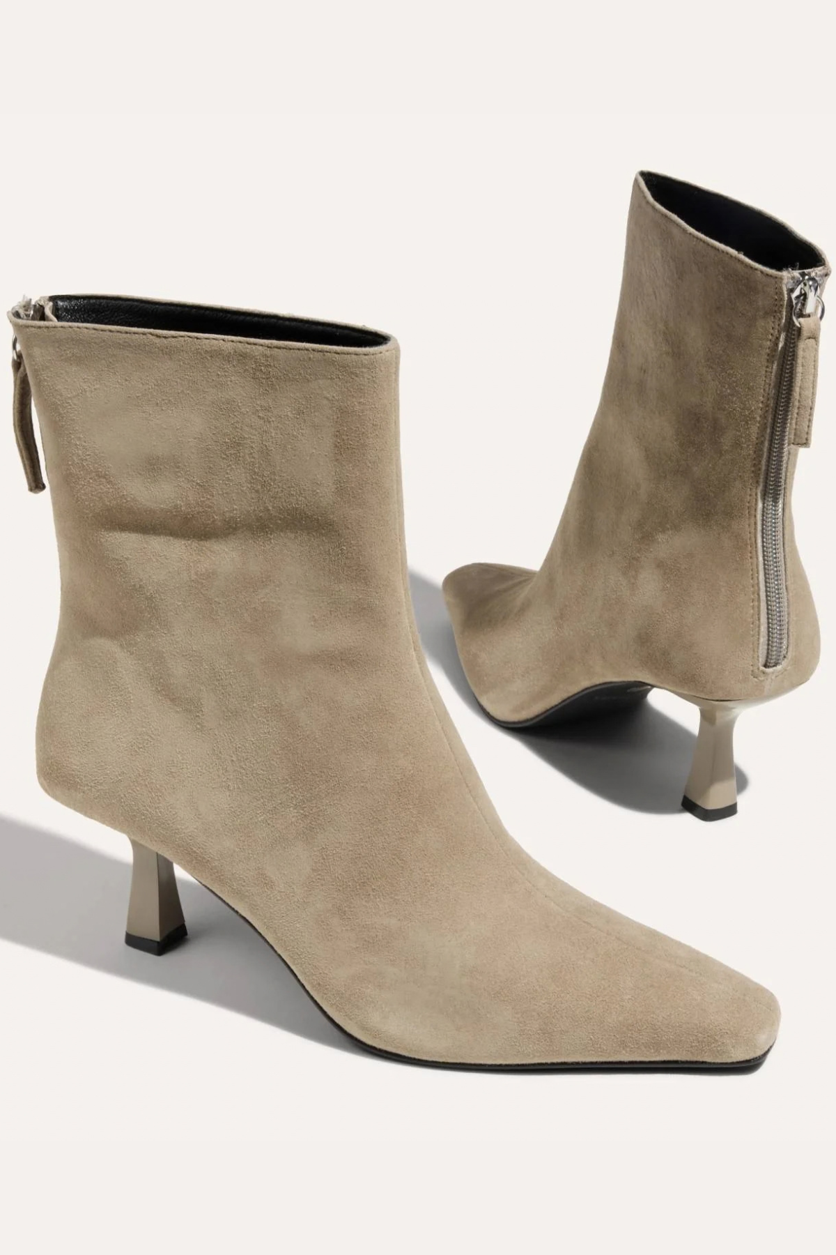 A pair of taupe suede ankle boots with pointed toes and kitten heels, shown from the side and back on a light beige background.