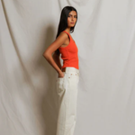 Woman wearing an orange top and white pants against a plain background