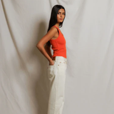 Woman wearing an orange top and white pants against a plain background