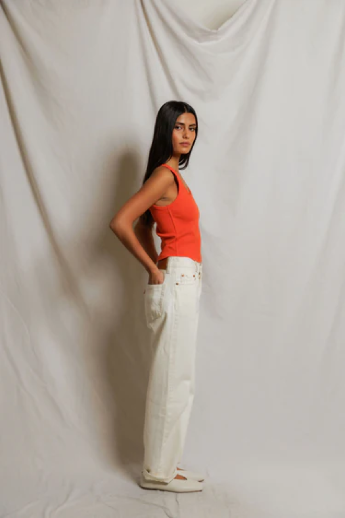 Woman wearing an orange top and white pants against a plain background