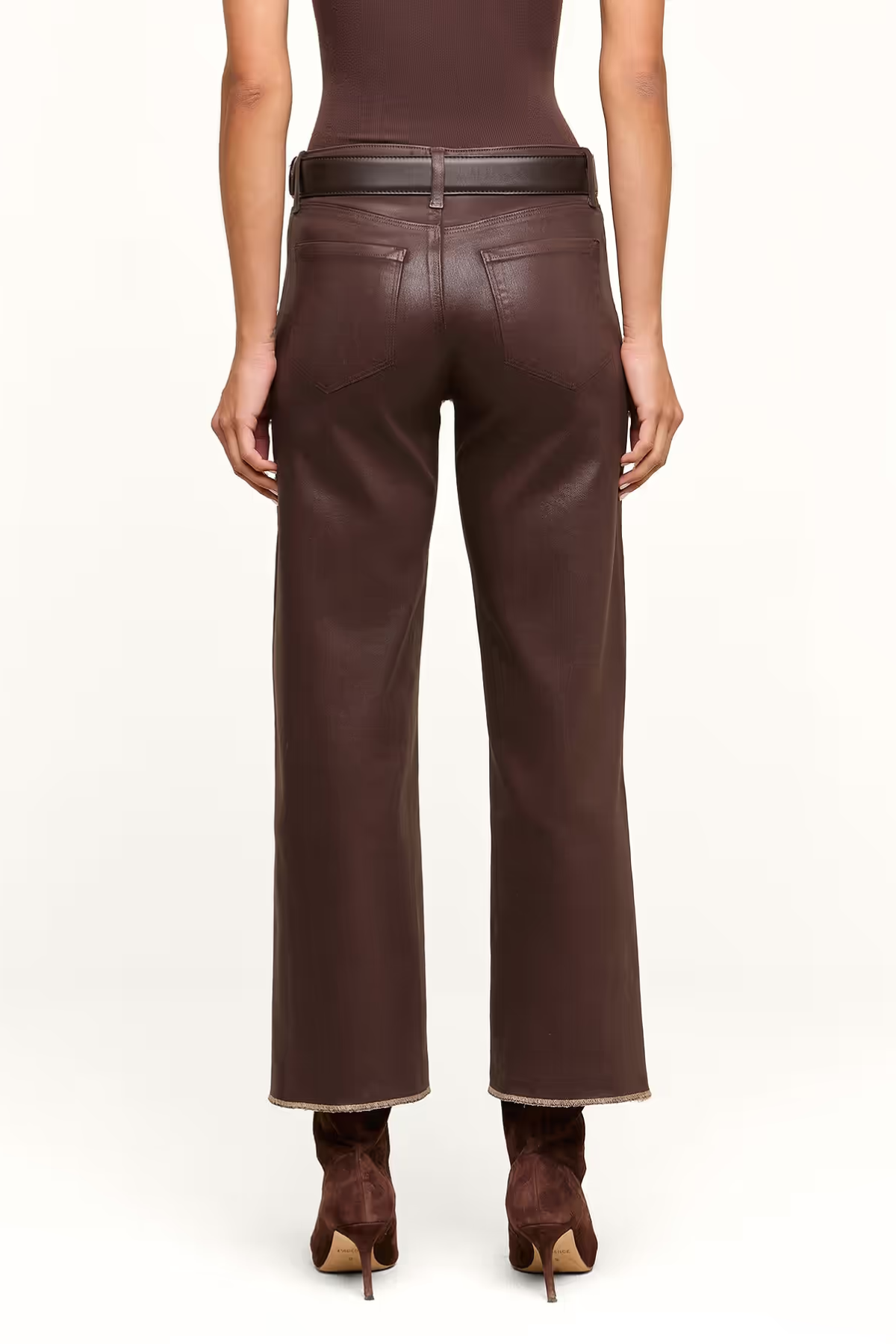 Rear view of a model wearing dark brown wide-leg faux-leather pants with a matching dark brown belt, paired with a dark brown top and brown ankle boots, against a plain white studio background.