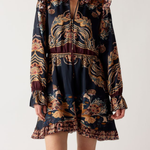A model wearing a dark navy blue mini dress with a complex gold, brown, and burgundy bohemian-style print, paired with burgundy knee-high boots, against a plain light gray background.