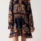 A model wearing a dark navy blue mini dress with a complex gold, brown, and burgundy bohemian-style print, paired with burgundy knee-high boots, against a plain light gray background.