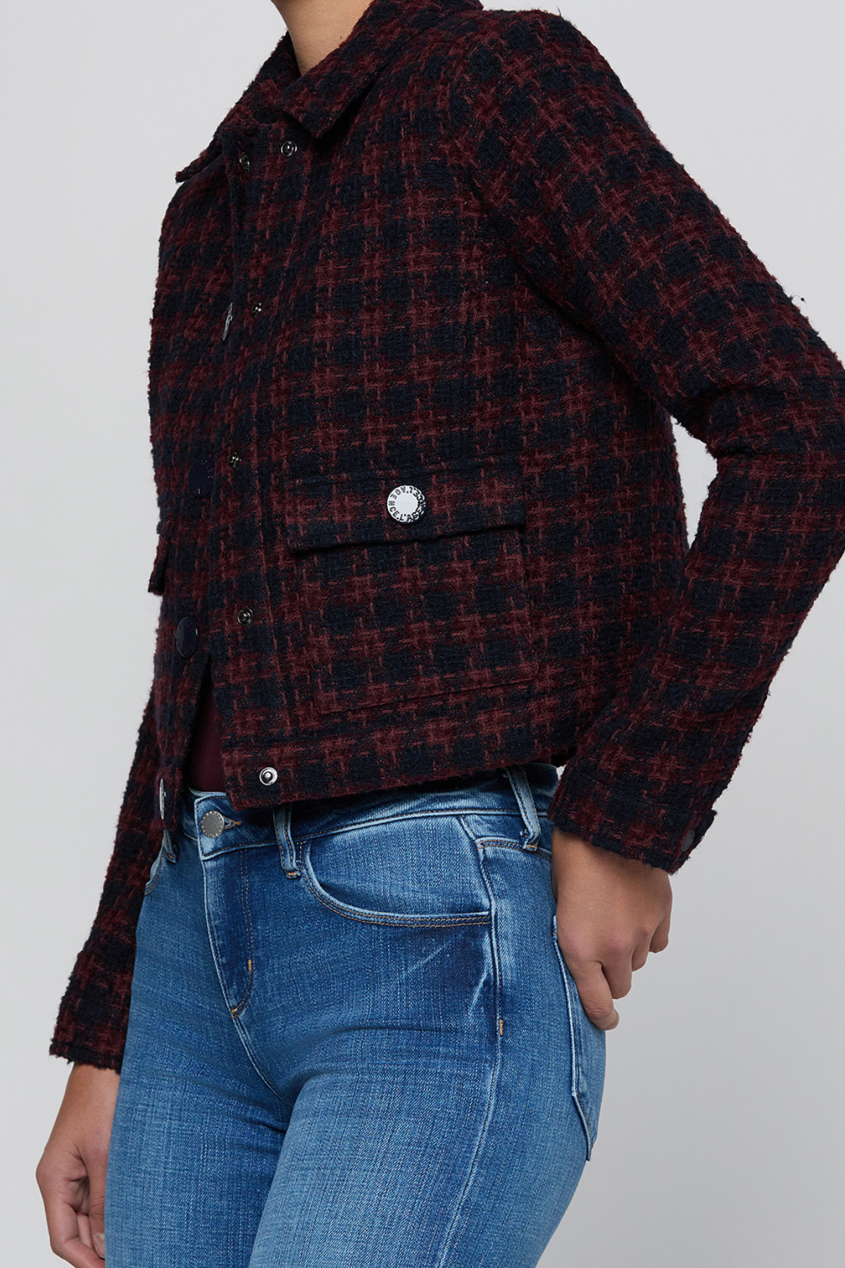 A cropped, long-sleeve plaid jacket in a dark red and black tweed-like fabric, worn by a model with blue jeans against a light gray background.
