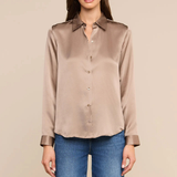 A woman modeling a taupe satin button-down shirt with blue jeans, standing against a solid beige background.
