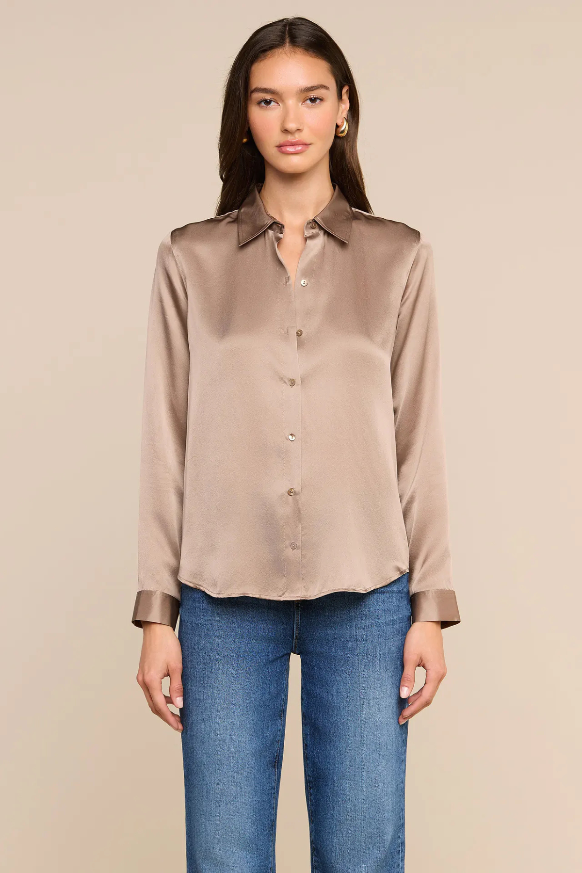 A woman modeling a taupe satin button-down shirt with blue jeans, standing against a solid beige background.