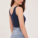 A woman wearing a navy blue sleeveless top and light blue jeans, shown from a side-back angle against a plain light background.