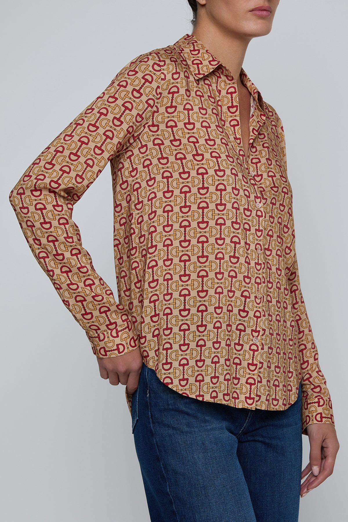 Person wearing a patterned shirt with long sleeves and blue jeans on a plain background