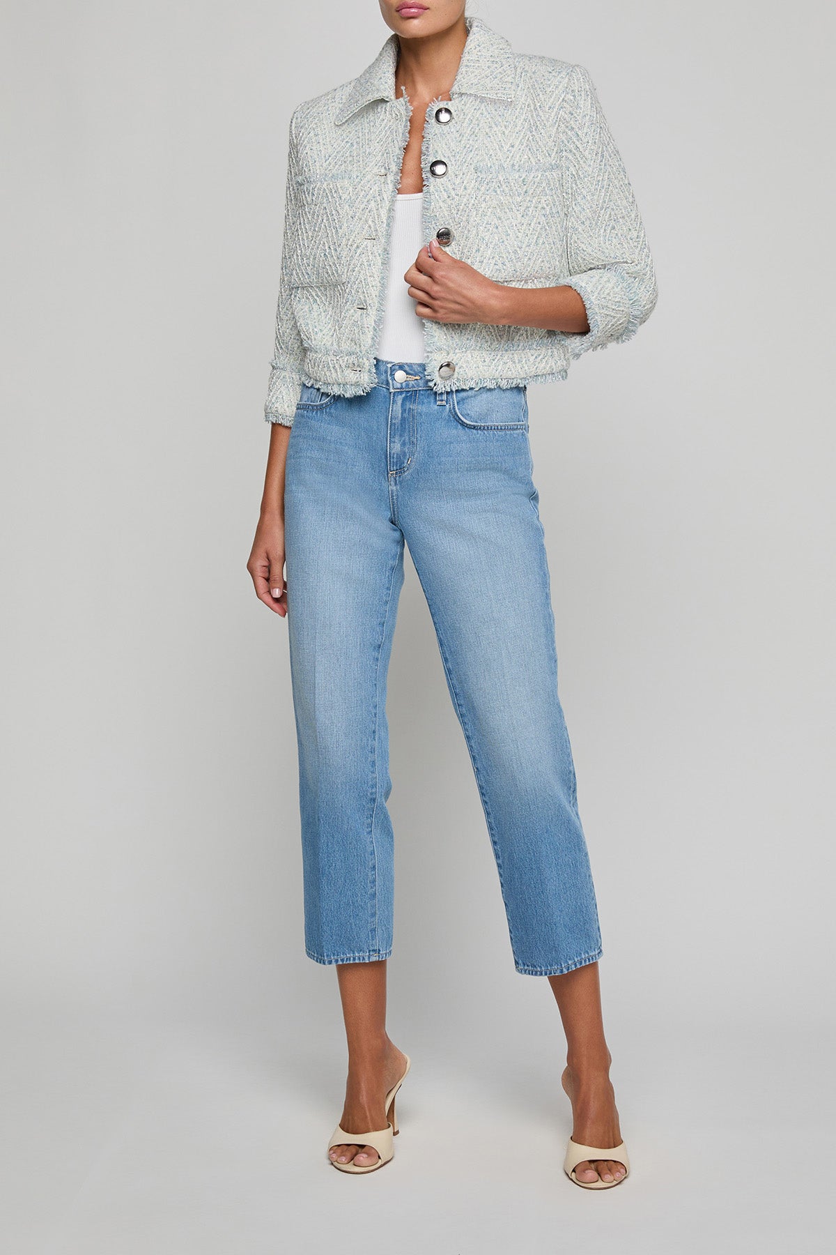 Person wearing a light gray textured jacket, white top, and blue jeans on a plain background