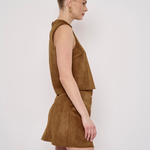 A woman in side profile wearing a sleeveless brown faux-suede romper with a matching mini skirt, set against a plain light gray studio background.