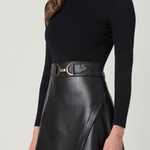 A woman wearing a black ribbed long-sleeve mock neck top and a black faux-leather A-line skirt with a wide waistband and gold horsebit belt, shown against a light gray studio background.