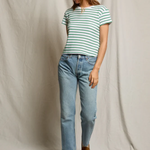 Woman wearing a striped shirt and jeans standing against a plain background