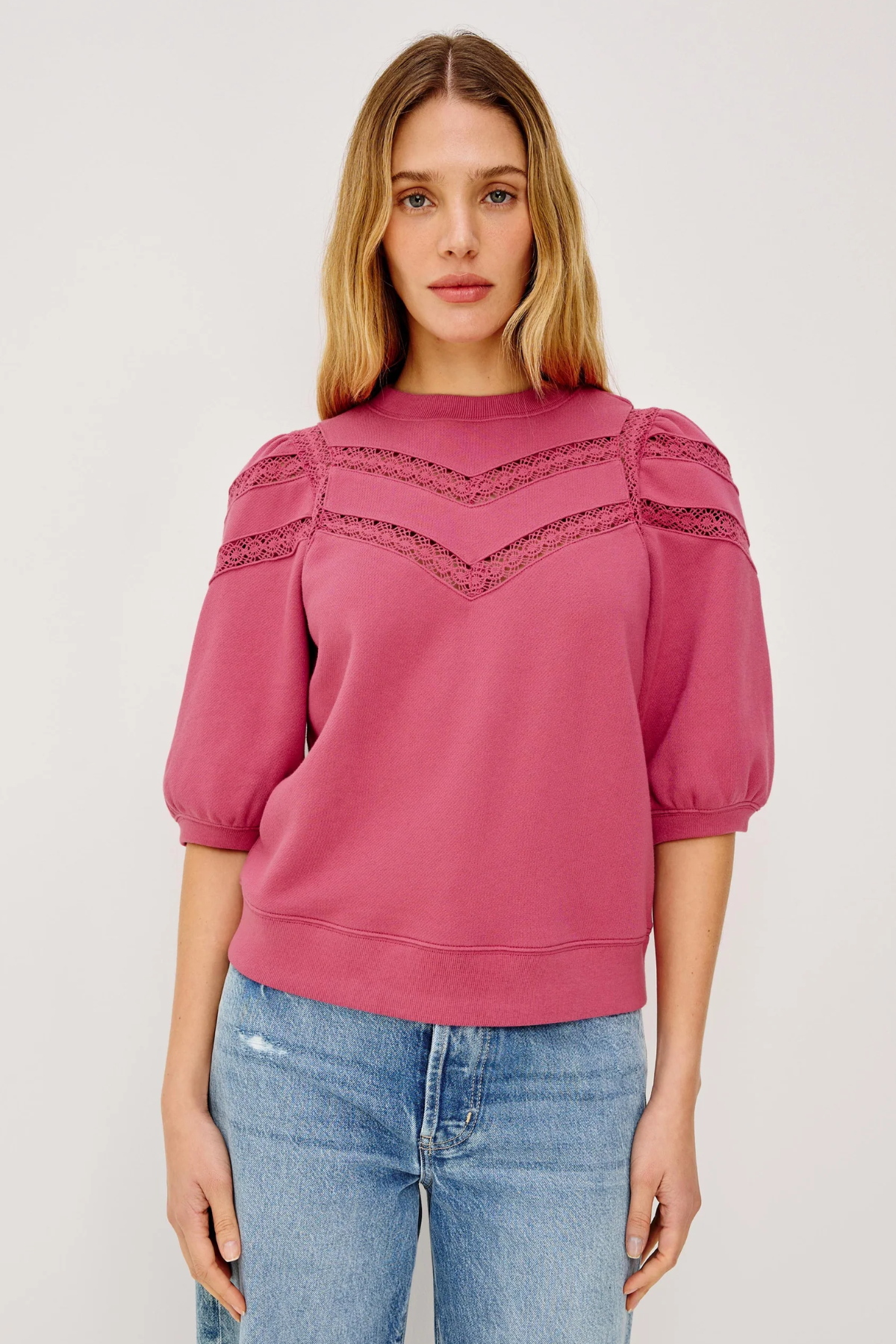 Woman wearing a pink blouse with lace details on a white background