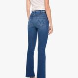 A woman shown from the back wearing blue high-rise flare jeans, a cream short-sleeve top, and metallic high heels against a plain white background.