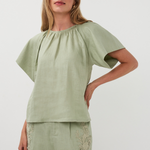 Woman wearing a green top and shorts with lace details on a white background