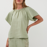 Woman wearing a green top and shorts with lace details on a white background