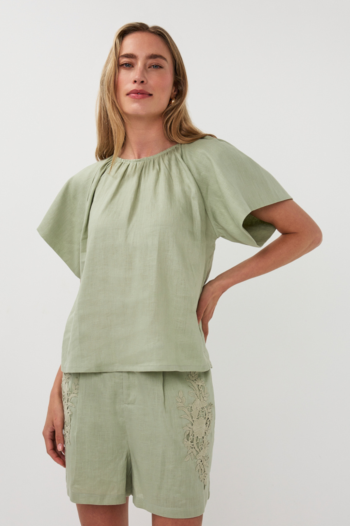 Woman wearing a green top and shorts with lace details on a white background