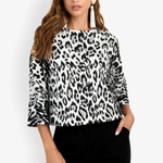 A woman modeling a black and white leopard print long-sleeve top with flared cuffs, paired with black pants, against a plain white studio background.