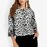 A woman modeling a black and white leopard print long-sleeve top with flared cuffs, paired with black pants, against a plain white studio background.
