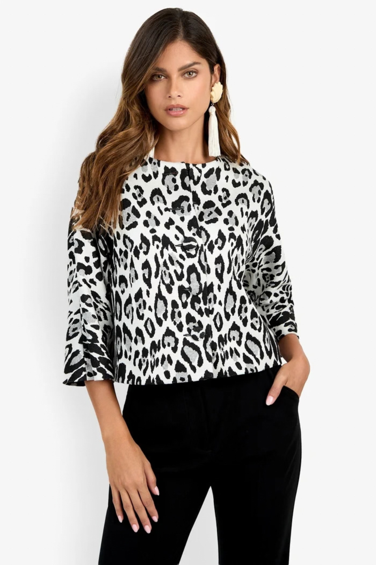 A woman modeling a black and white leopard print long-sleeve top with flared cuffs, paired with black pants, against a plain white studio background.
