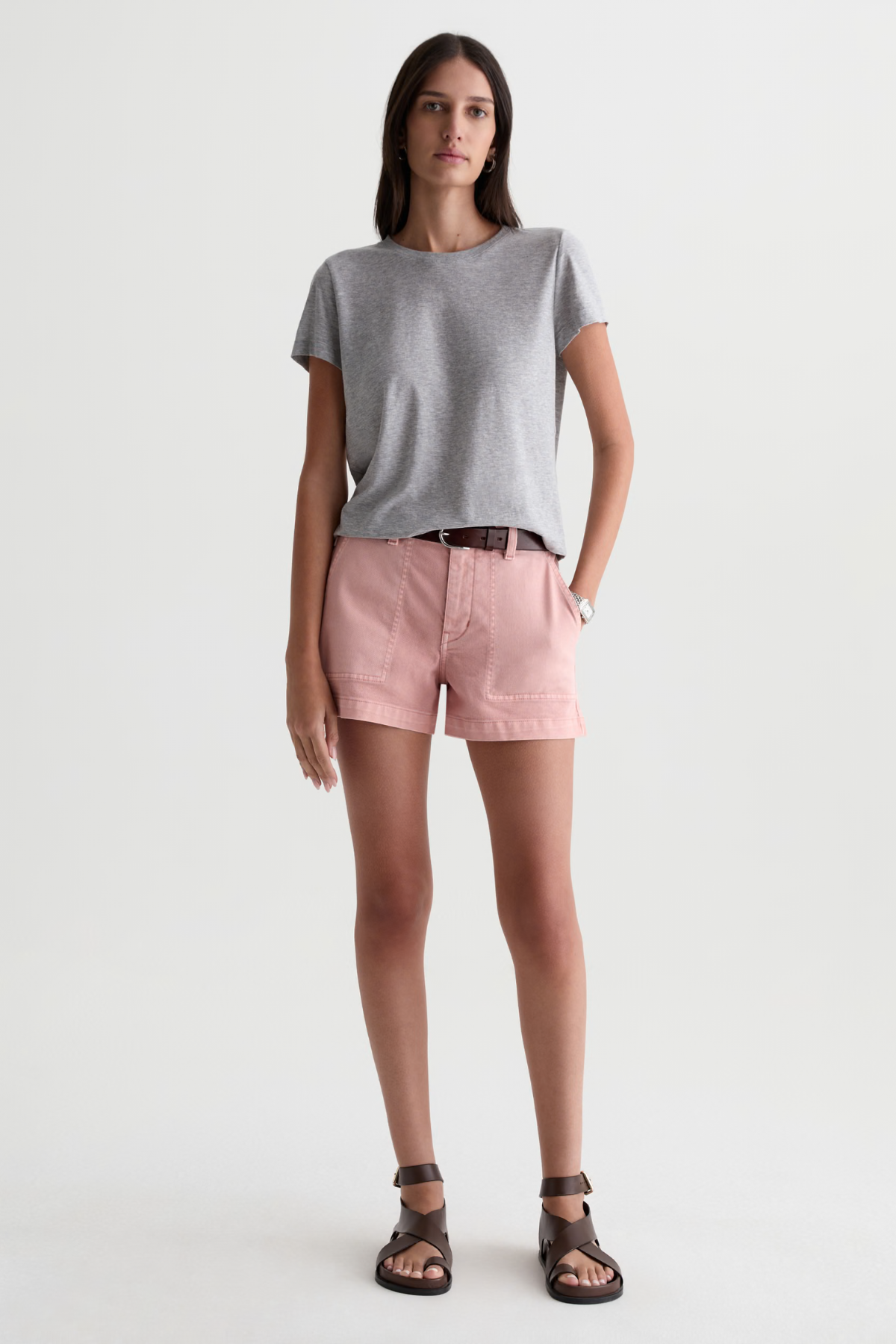 A woman modeling a light gray short-sleeve t-shirt and dusty pink shorts against a plain white studio background.