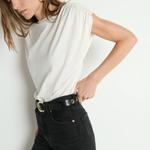 Woman wearing a white top and black pants against a plain background