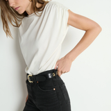 Woman wearing a white top and black pants against a plain background