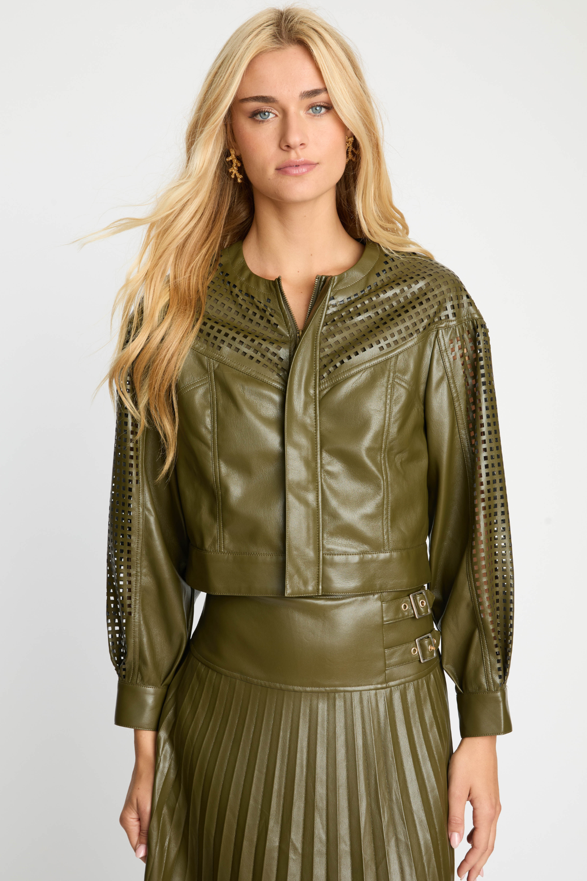 Woman wearing a green leather jacket with decorative cutouts on a white background