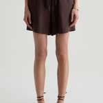 A model wearing dark brown drawstring shorts and matching strappy flat sandals, shown from the waist down against a light gray studio background.