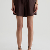 A model wearing dark brown drawstring shorts and matching strappy flat sandals, shown from the waist down against a light gray studio background.