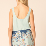 Woman wearing a light blue sleeveless top and floral skirt on a beige background