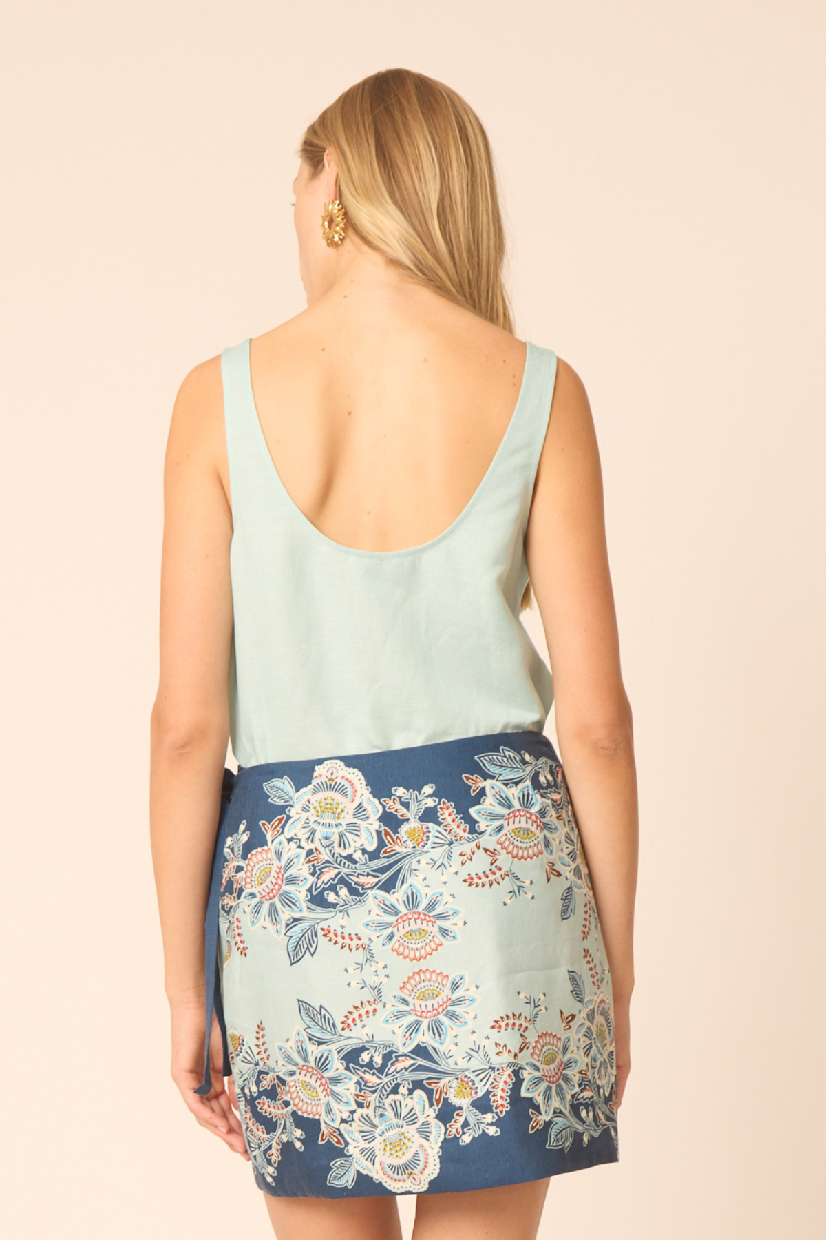 Woman wearing a light blue sleeveless top and floral skirt on a beige background