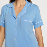 Woman wearing a light blue pajama top with white trim on a plain background